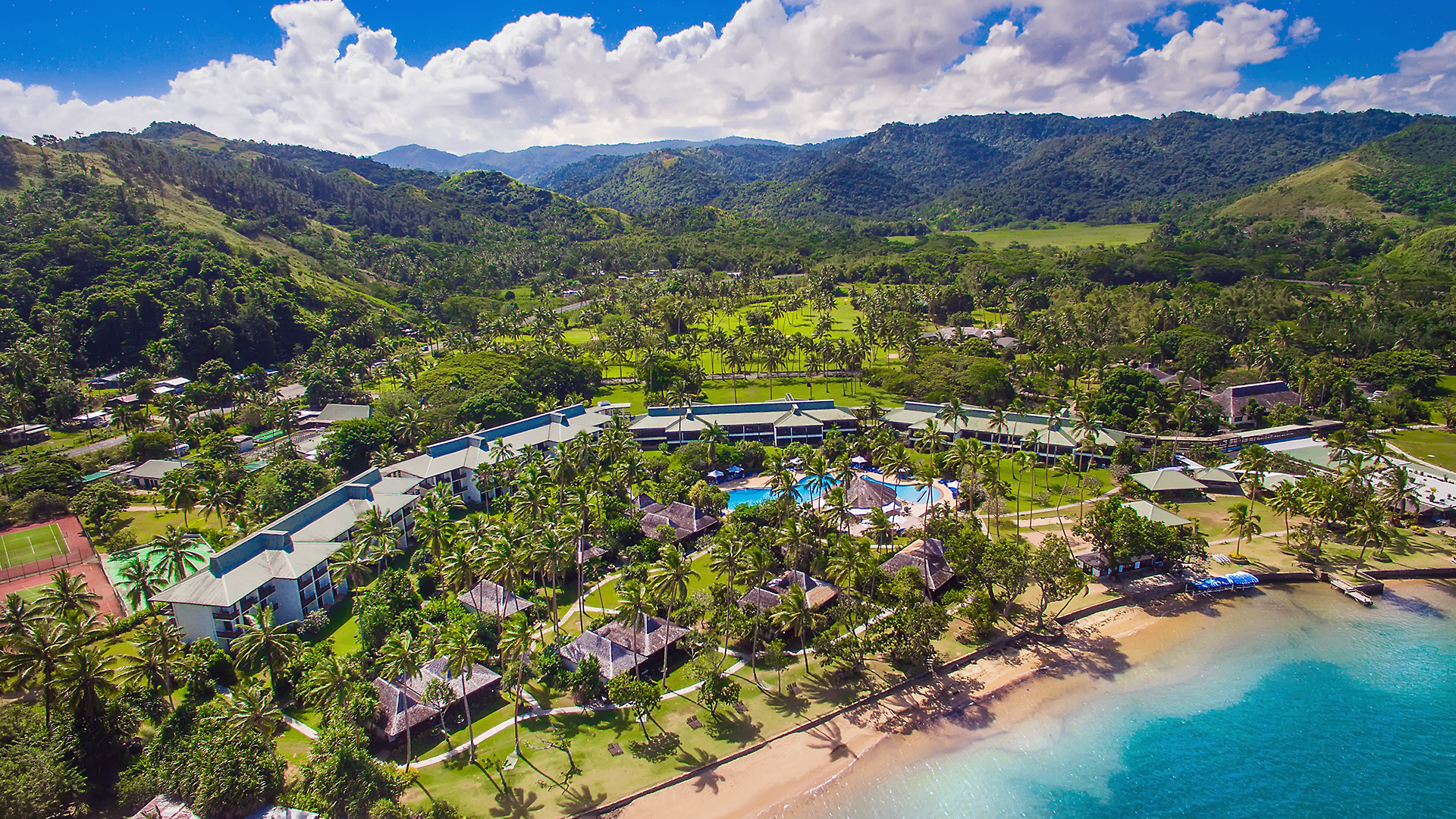 Aerial view of The Naviti Resort beachfront, pool and palm-lined grounds